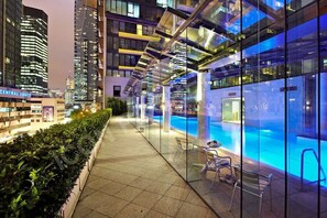 A modern hotel with a glass-enclosed infinity pool, a rooftop terrace, and a city view.