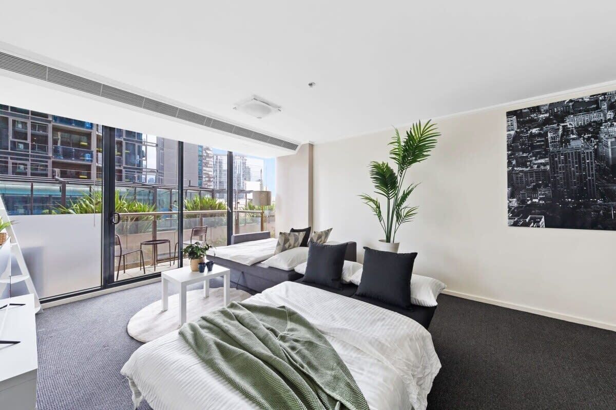 A modern hotel room with a large bed, a balcony with a city view, and a potted plant.
