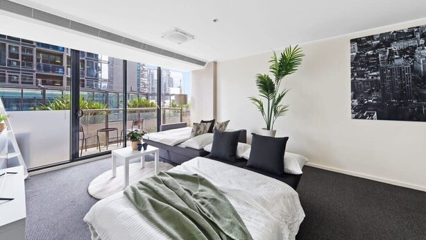 A modern hotel room with a large bed, a balcony with a city view, and a potted plant. - A Large 2BR Apt Near Crown, Sleeps 8, FREE Parking (Southbank)