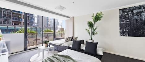 A modern hotel room with a large bed, a balcony with a city view, and a potted plant.
