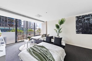 A modern hotel room with a large bed, a balcony with a city view, and a potted plant.