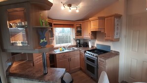 A compact kitchen with wooden cabinets, a gas stove, a sink, and a window with a view of the outside.