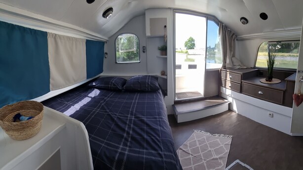 A compact, well-lit interior with a bed, a small seating area, and a window offering a view of the outdoors.