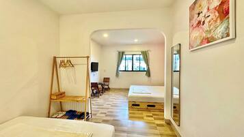 A room with two beds, a wooden rack, a TV, and a painting.