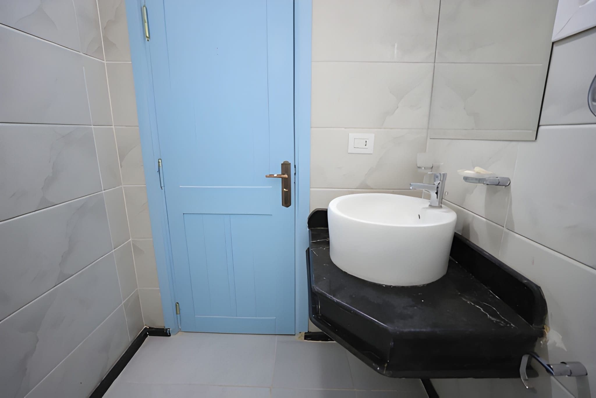 A bathroom with a blue door, a white sink, and a black countertop.