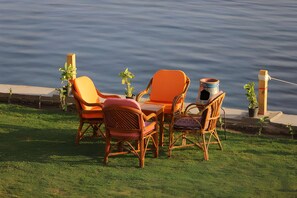 An outdoor seating area with wicker chairs and a table, overlooking a body of water. - Noprea Boutique Hotel (Aswan)