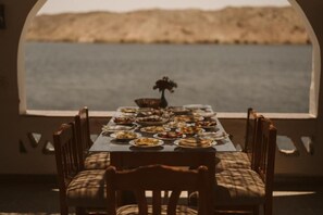 Mesa de comedor servida con diversos platos, ubicada frente a una ventana con vista al agua.