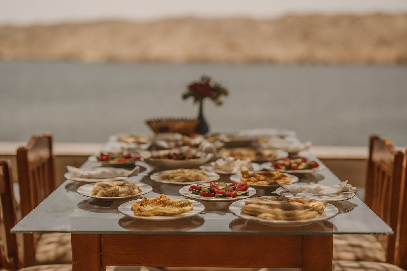 Mesa de comedor dispuesta con varios platos, sillas y vista a una masa de agua.