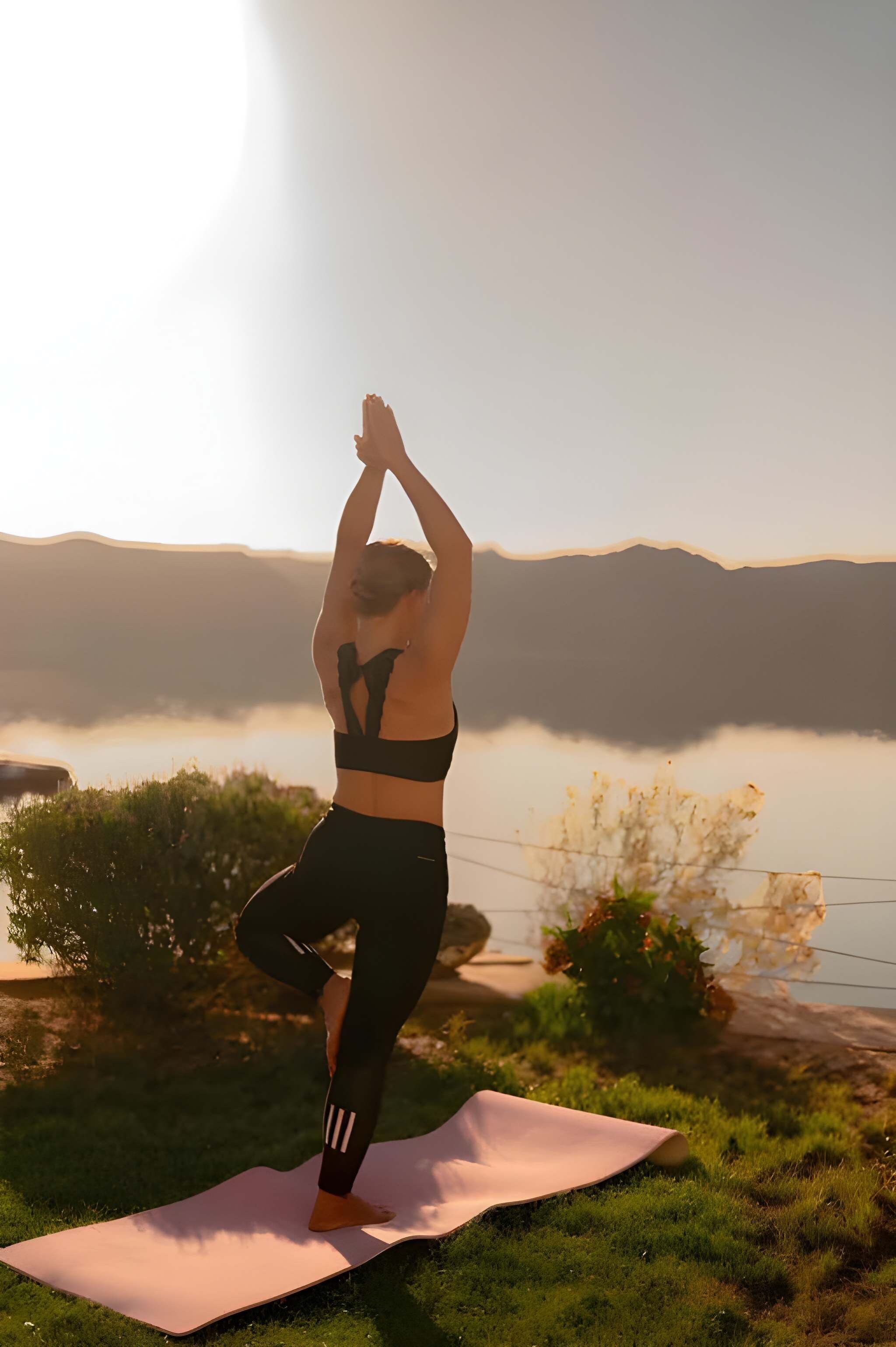 A person practicing yoga on a mat with a scenic view of mountains and a body of water in the background.