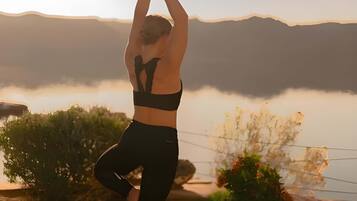 A person practicing yoga on a mat with a scenic view of mountains and a body of water in the background.
