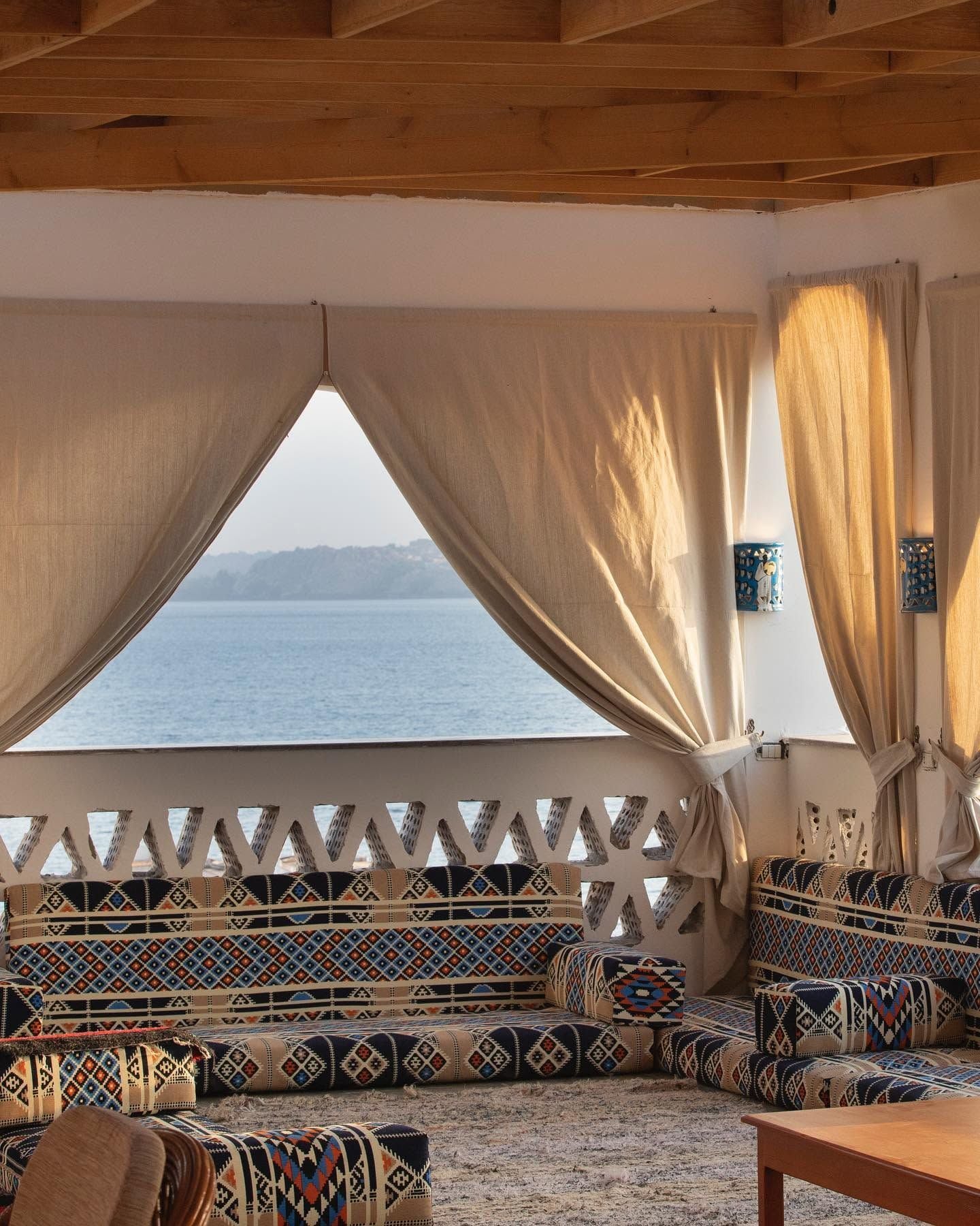 Habitación con vista al mar, que cuenta con techo de madera, un sofá estampado y una mesa.