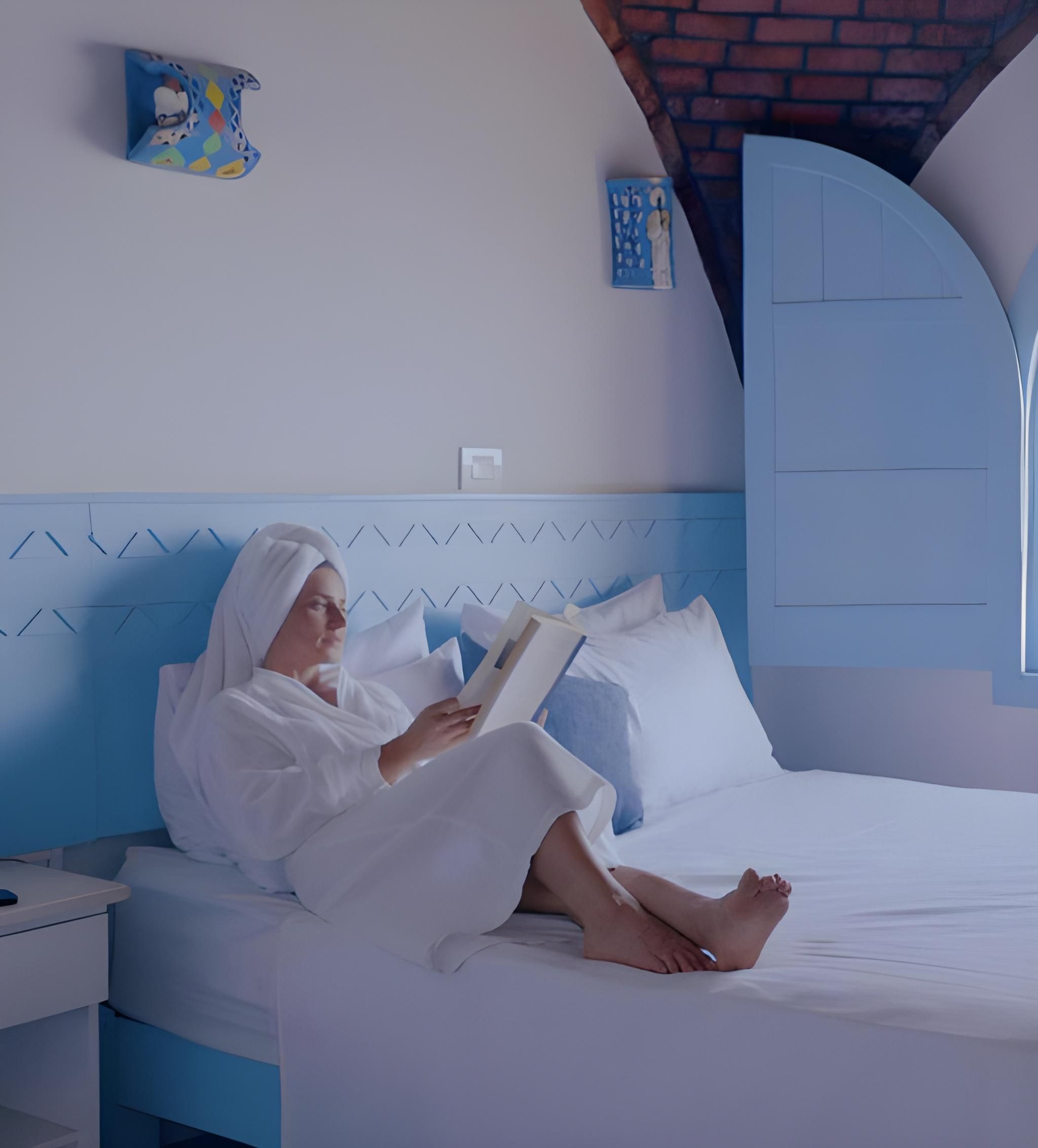 Una persona acostada en una cama con cabecera azul, leyendo un libro.