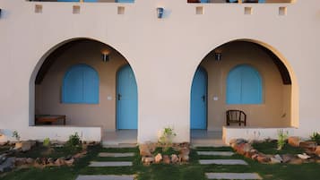 Um edifício com duas arcadas simétricas que levam a portas, uma pequena área de estar e um jardim com pedras para caminhar.