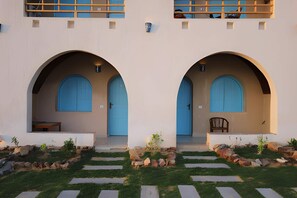 A building with two symmetrical archways leading to doorways, a small seating area, and a garden with stepping stones. - Noprea Boutique Hotel (Aswan)