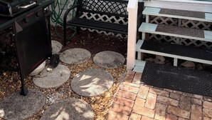 Une terrasse avec un réchaud à gaz, une chaise verte, une porte blanche et un chemin en briques.