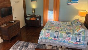 Une chambre à coucher avec un lit, une commode, une table de chevet, un téléviseur et une fenêtre avec des rideaux.