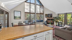 A spacious living area with a large wooden dining table, a fireplace, and a cozy seating area. - Wooded Chalet w Hot Tub & Indoor Pool / Gym Access (Hedgesville)