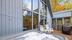 A hot tub on a wooden deck with a view of a modern building and trees. - Wooded Chalet w Hot Tub & Indoor Pool / Gym Access (Hedgesville)