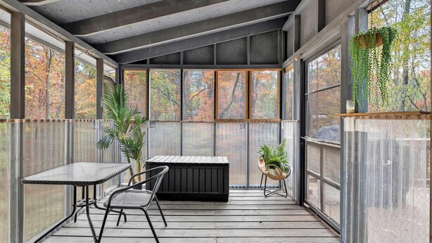 A covered outdoor area with a table and chairs, a black bench, and potted plants. - Wooded Chalet w Hot Tub & Indoor Pool / Gym Access (Hedgesville)