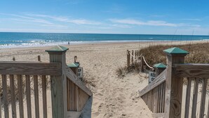 A wooden beach gate leading to a sandy beach with a clear view of the ocean.