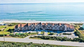 A multi-story hotel with a central courtyard, located near a beach with a clear view of the ocean.