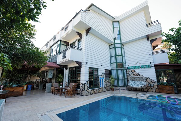 A modern hotel with a swimming pool, outdoor seating, and a stone facade.