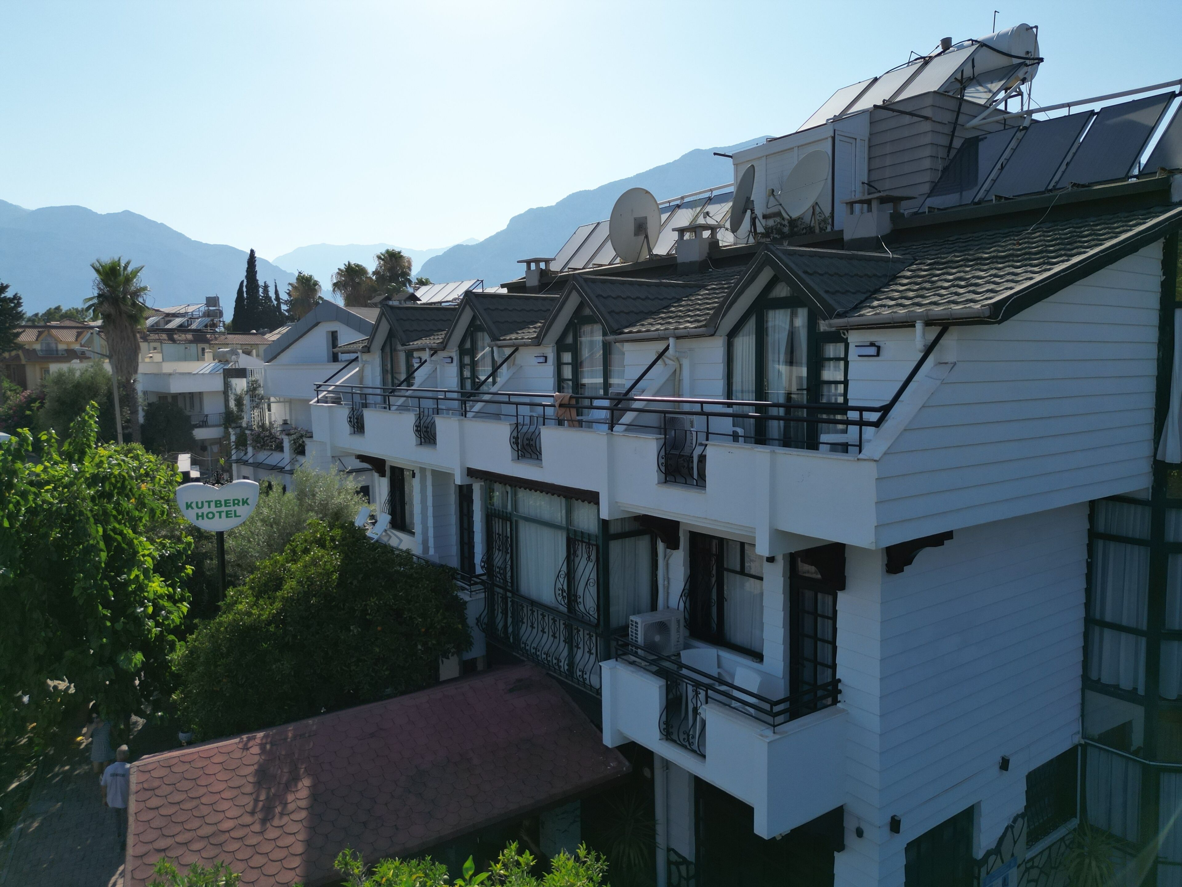 A hotel with multiple balconies, satellite dishes, and a mountainous backdrop.
