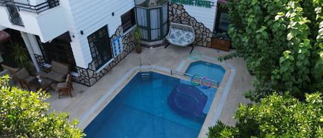 A hotel with a swimming pool, outdoor seating, and a stone facade.