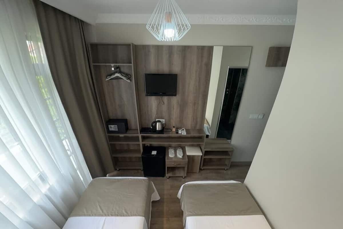 A hotel room with two beds, a desk with a TV, a coffee machine, and a wardrobe.
