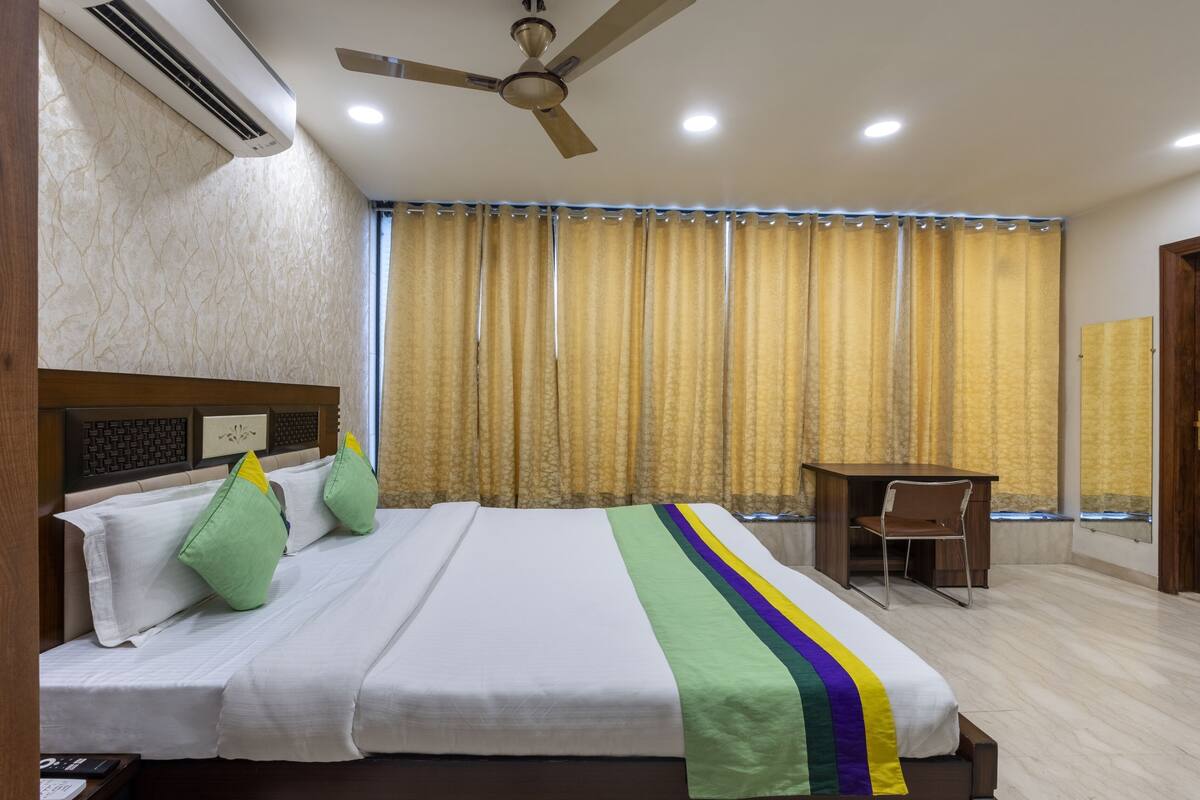 A hotel room with a bed, a ceiling fan, an air conditioner, a desk, and a chair.
