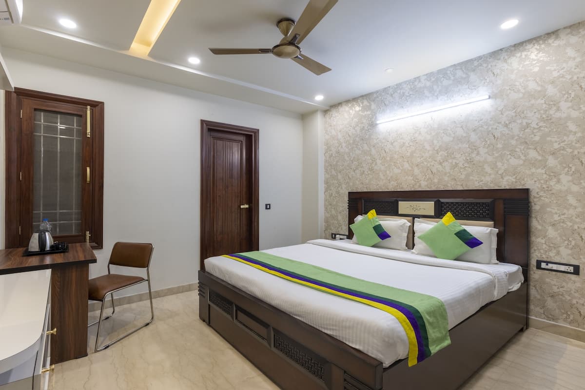 A hotel room with a bed, a desk, a chair, a ceiling fan, and a TV.