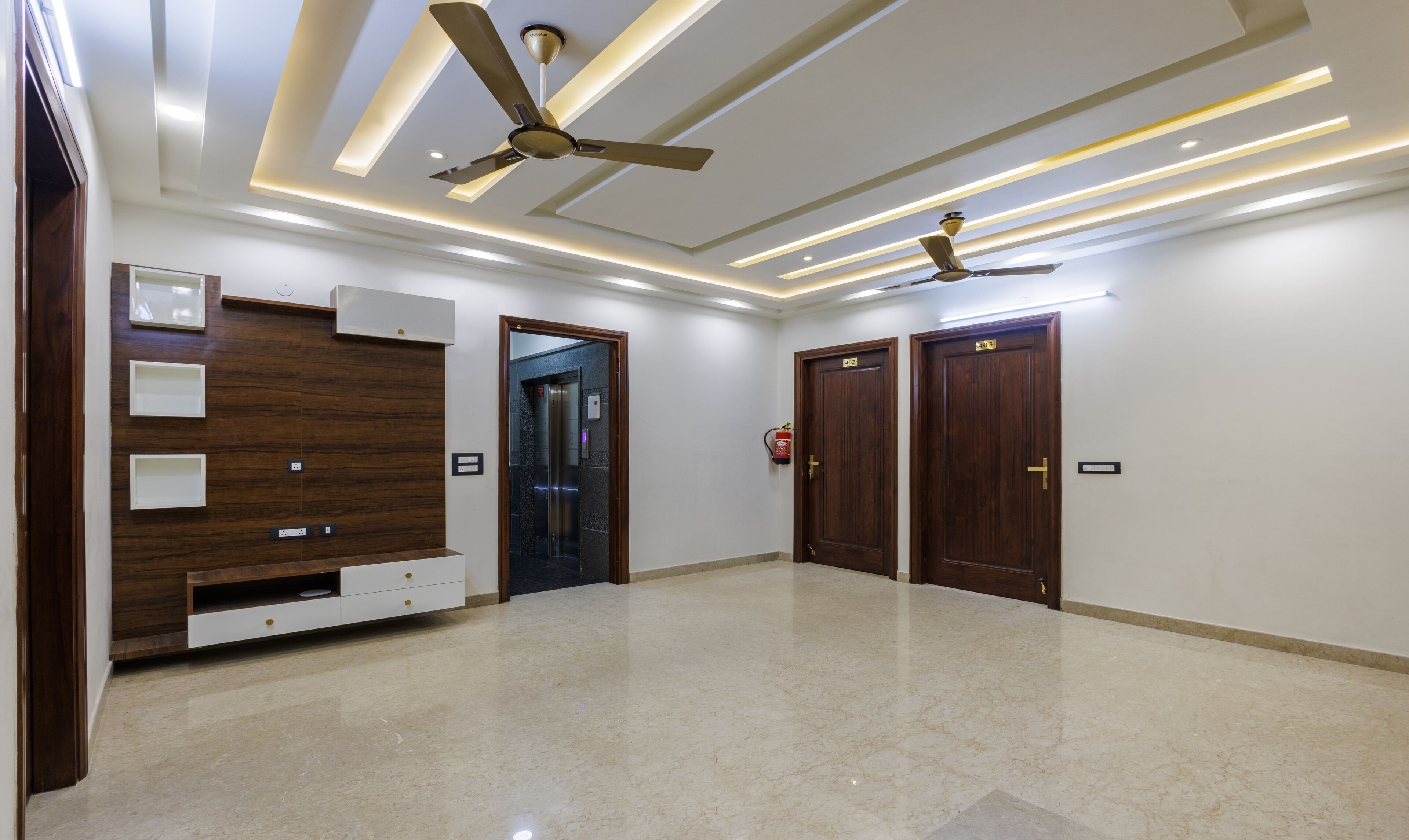 A spacious hallway with two wooden doors, a ceiling fan, recessed lighting, and a marble floor.