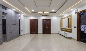 A hallway with marble flooring, wooden doors, and a ceiling fan. - Treebo MVM Residency (New Delhi)