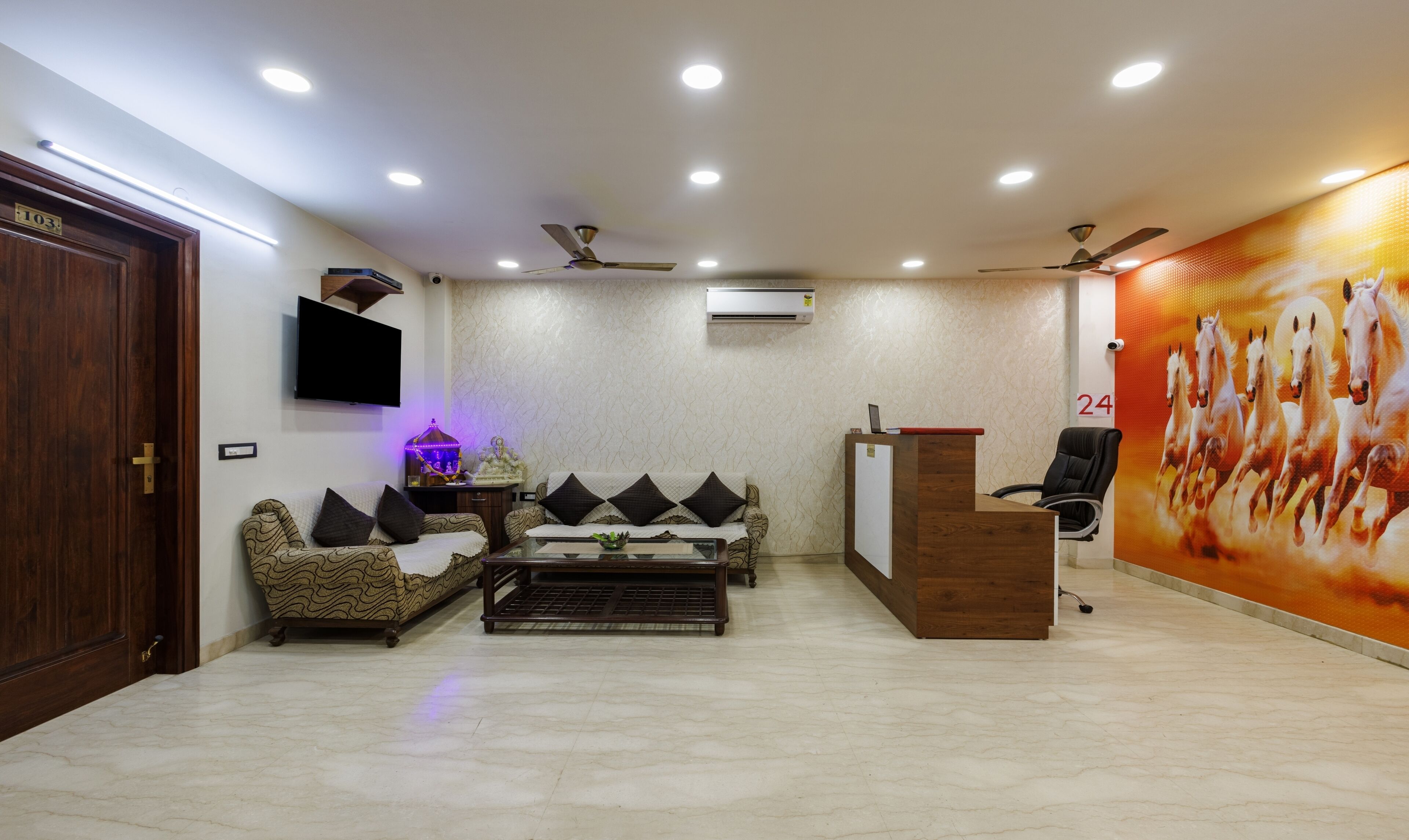 A modern office space with a reception desk, a sofa set, a television, and a ceiling fan.