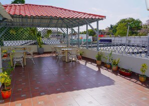 Un espacio cubierto con patio, suelo de baldosas, mobiliario exterior y plantas en macetas.