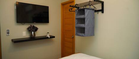 Un dormitorio con cama, televisor montado, estante con un jarrón y una puerta.