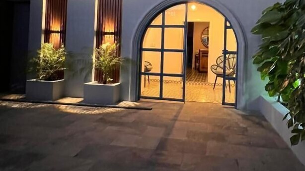 Un edificio moderno con una entrada arqueada grande, un letrero iluminado destacado y plantas en macetas alrededor del área de acceso.