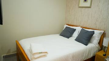 A neatly made bed with white and grey linens, a wooden headboard, and a small bedside table with a lamp.