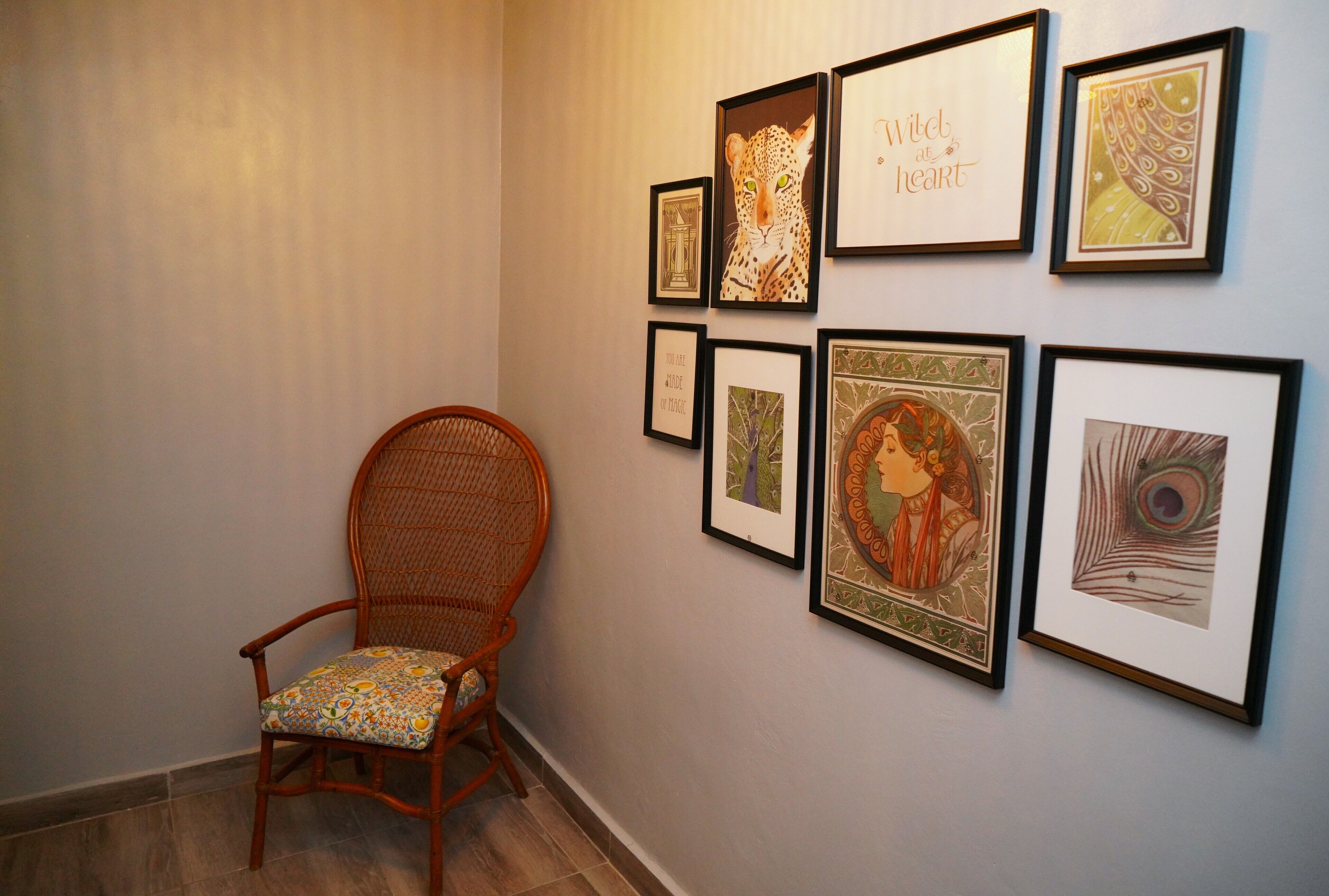 A hallway with a wicker chair and various framed artworks on the wall.