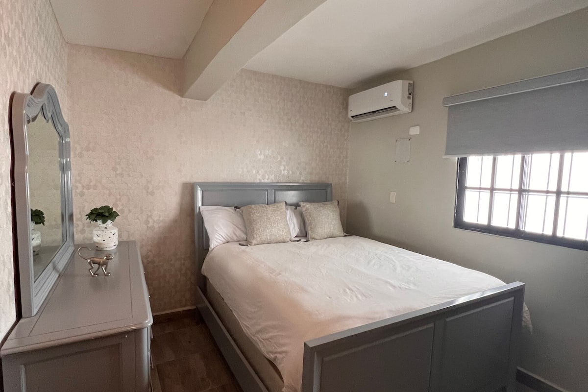 Een slaapkamer met een bed, een dressoir, een spiegel en een raam.
