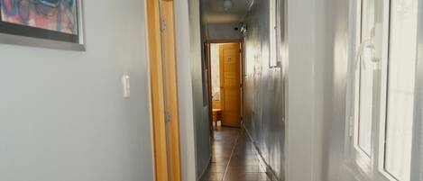 A hallway with a wooden floor, a framed abstract painting on the left, and a door with a 'No Smoking' sign.