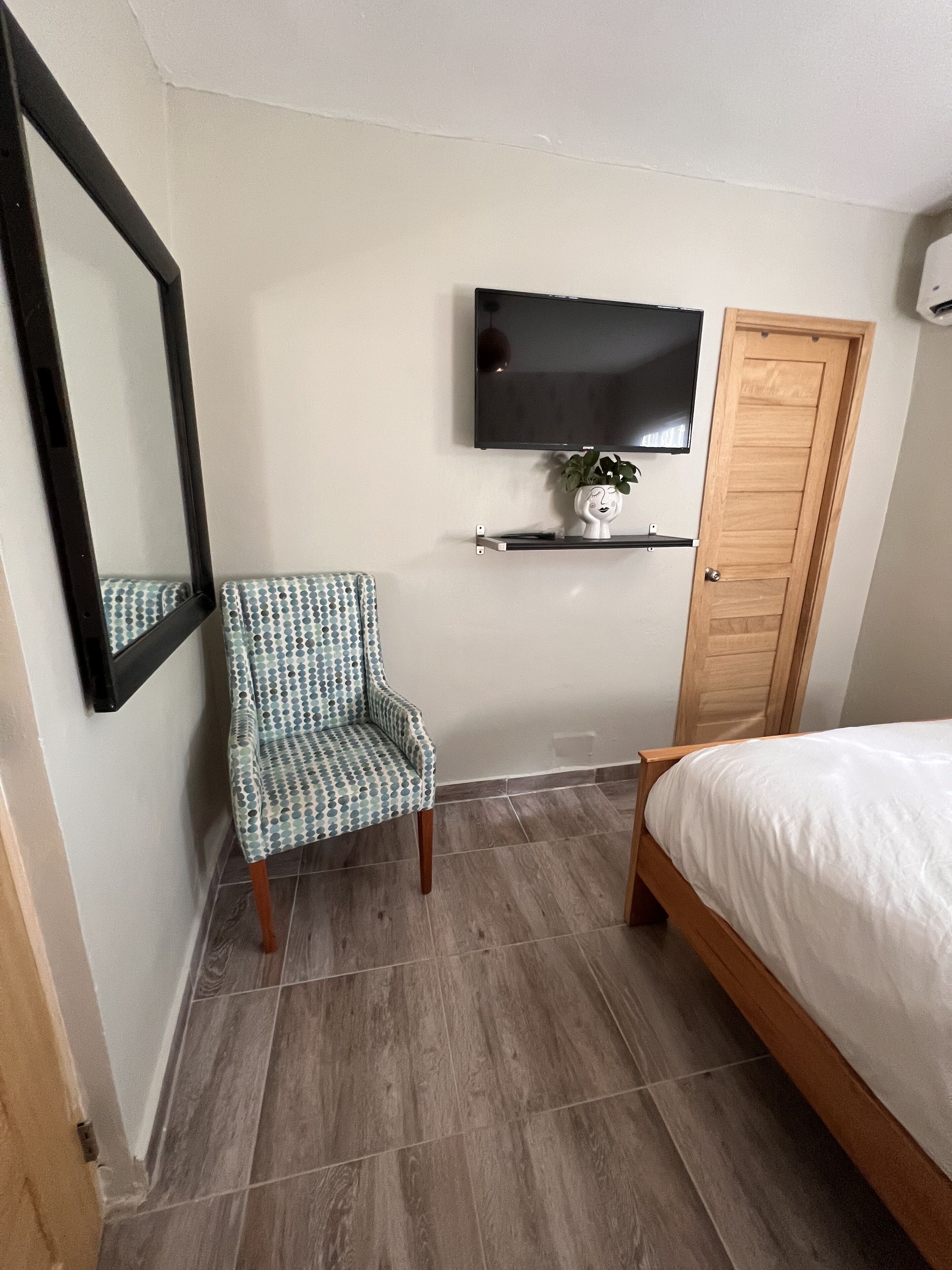 Een slaapkamer met een bed, een stoel, een aan de muur bevestigde televisie en een houten deur.