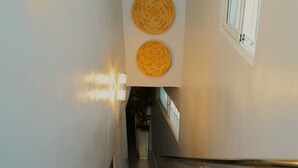 Una escalera de madera con barandilla, un aplique de pared y tres tapices tejidos.
