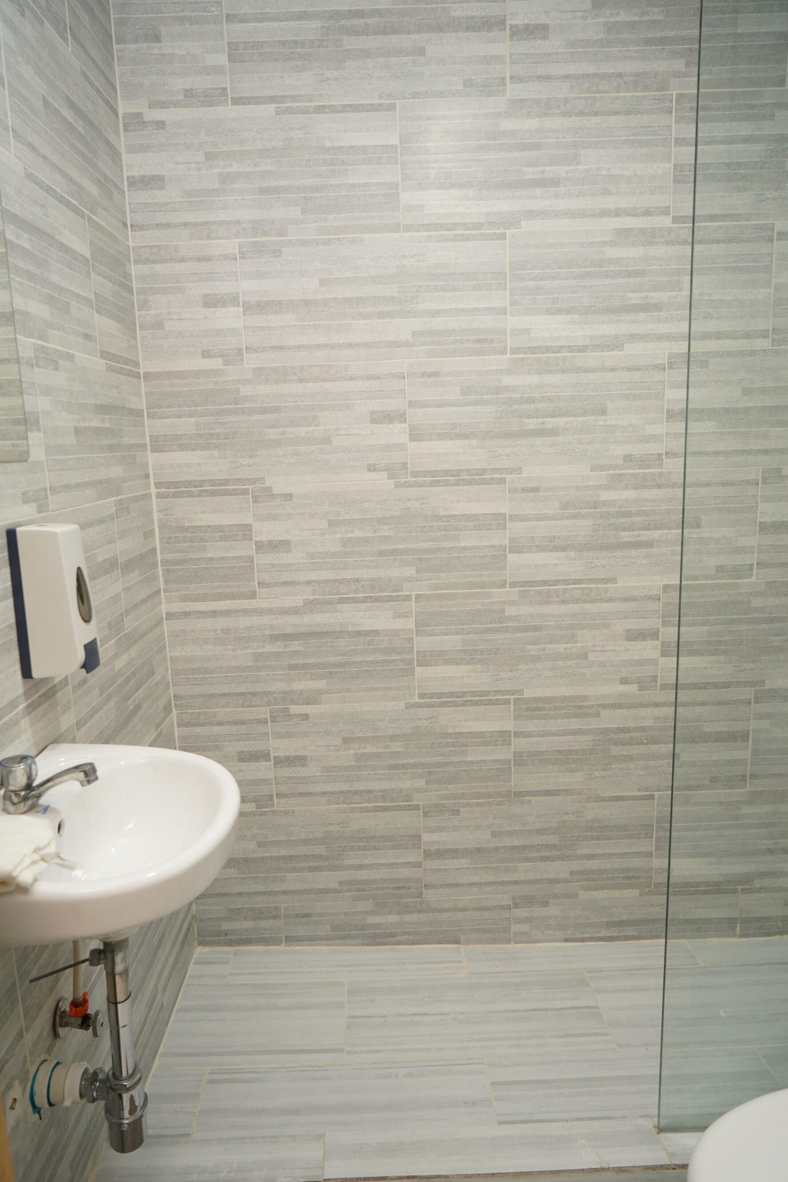 A bathroom with a white sink, a soap dispenser, and a tiled wall.
