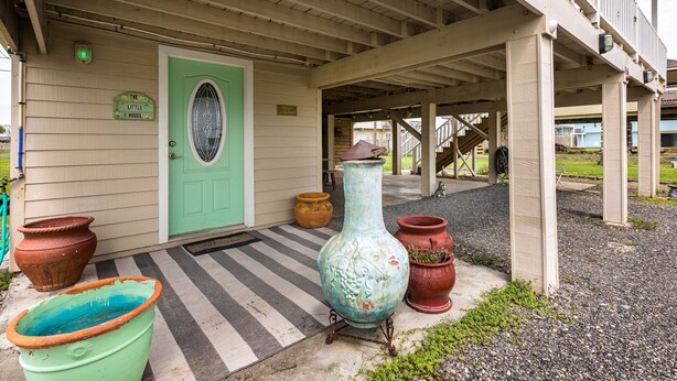 A porch with a green door, potted plants, and a staircase leading to an upper level.