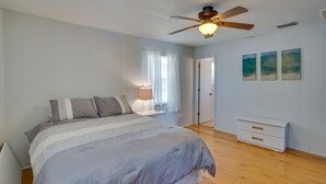 Un dormitorio con cama, mesita de noche, cómoda, ventilador de techo y tres cuadros colgados en la pared.