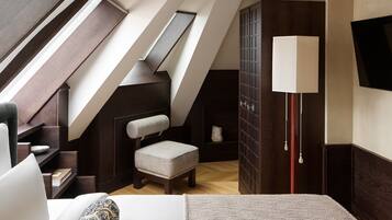 A bedroom with a sloped ceiling, a chair, a bedside table, a lamp, and a wardrobe.