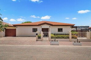 Una casa de dos pisos con techo de tejas rojas, entrada con portón y camino de entrada pavimentado.