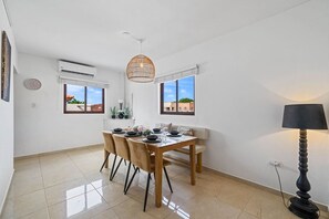 A dining area with a table set for two, a hanging light fixture, and a view through the window. - Felicidad: Stunning 3BR Retreat with Private Pool (Oranjestad)