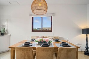 Un comedor con una mesa de madera dispuesta para cuatro, una lámpara colgante de mimbre y vistas al exterior.